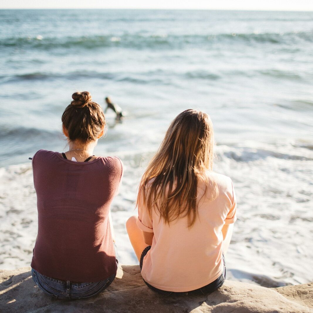 two women sitting on cliff looking at the ocean