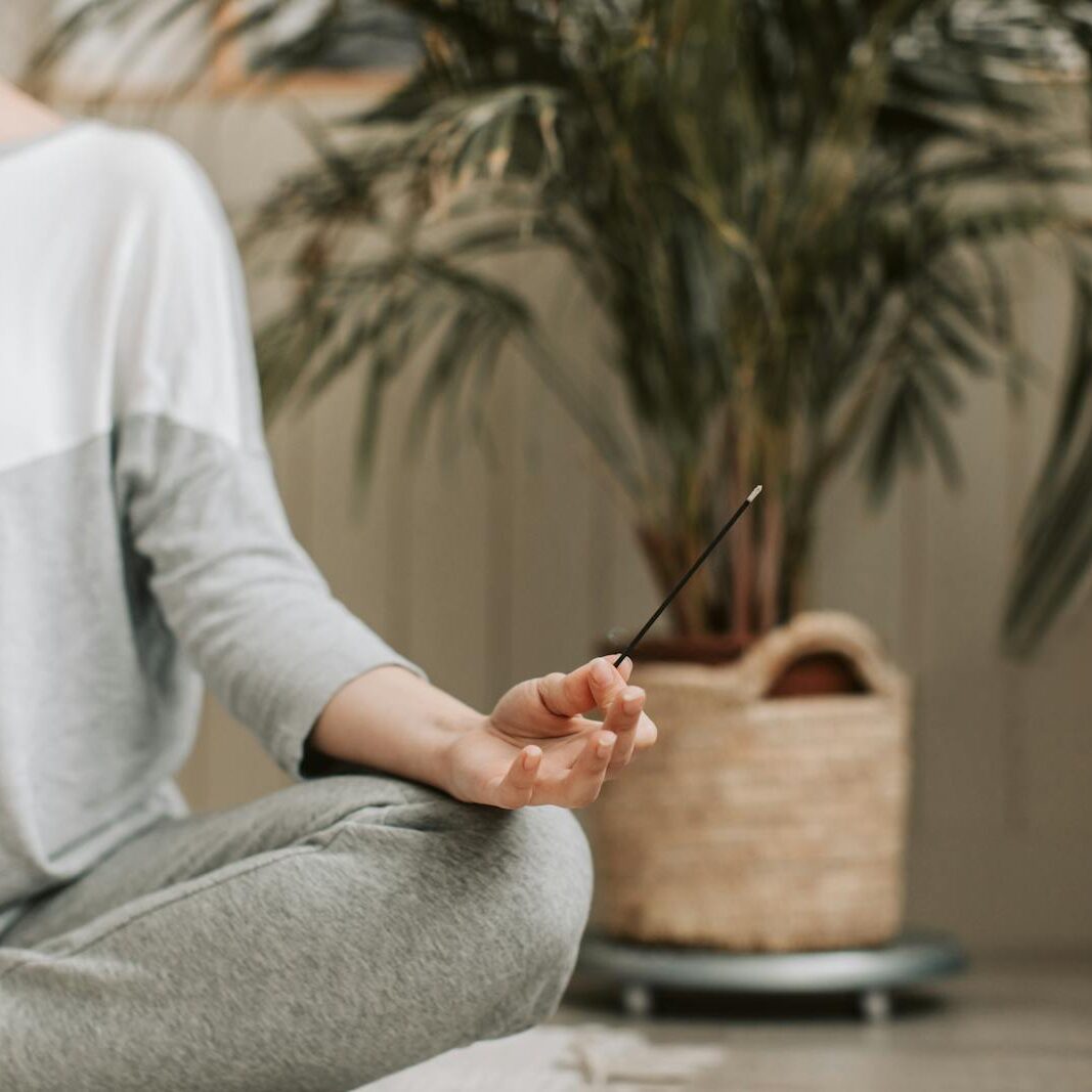 Woman meditating indoors holding incense, promoting relaxation and calm.