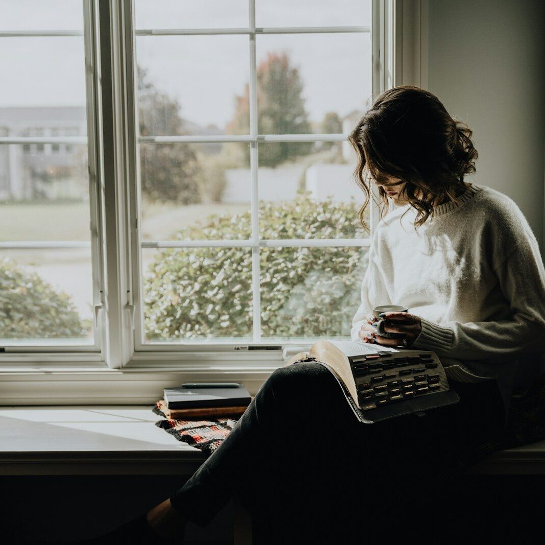 A woman sitting on a window sill reading a book